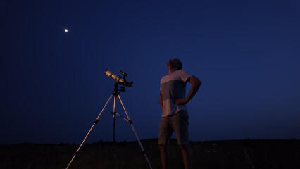 Amateur astronomer using telescope for watching stars, Moon, planets and other celestial objects from a field in nature.
