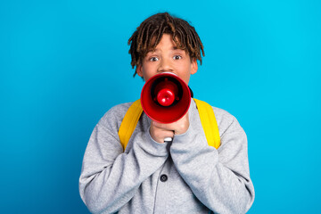 Charming student holding red megaphone with bright expression in front of blue background wearing...