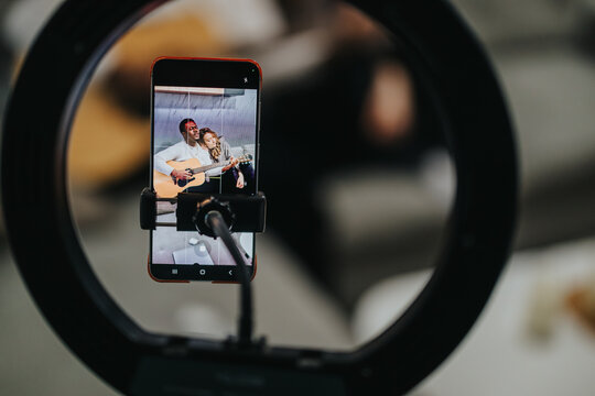 Smart phone secured within a ring light captures a live musical moment, highlighting musician playing the guitar, emphasizing creative technology and artistic expression in a modern and connected