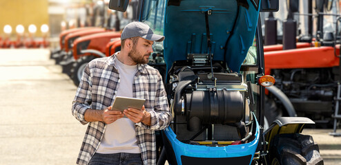 Technician performing tractor engine inspection in outdoor farm machinery lot