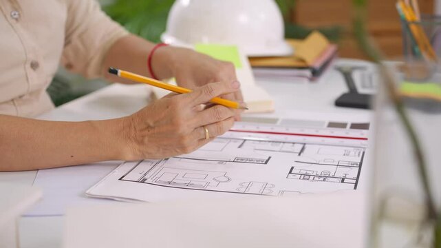 Detailed view of female hands pointing at architecture layout on paper with pencil