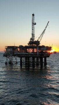Aerial shot of an offshore oil platform at sunset. Vertical Video.
