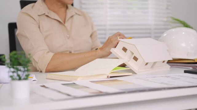 Elegant Asian woman reviewing architecture designs and sketches while seated in bright studio space