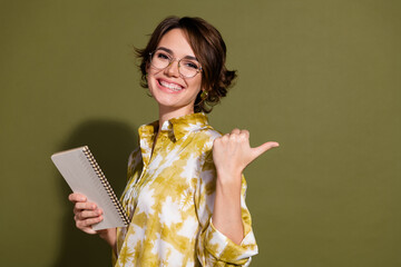 Confident young businesswoman in elegant blouse smiling and holding notebook against khaki...