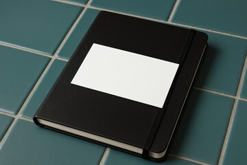 Black hardcover notebook with blank white label on blue tiles