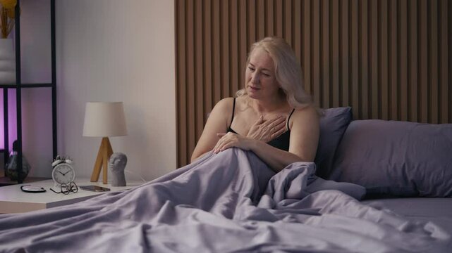 Middle-aged woman sitting in bed with strong chest pain, heart stroke risk