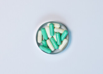 Close-up top-view of green and white capsule pills in a metal container on white background. Lay...