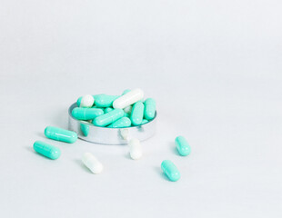 Selective focus of green-white capsule pills in a stainless container, scattered on a clean surface with copy space, showing modern healthcare, medication, and pharmaceutical supplement concept.