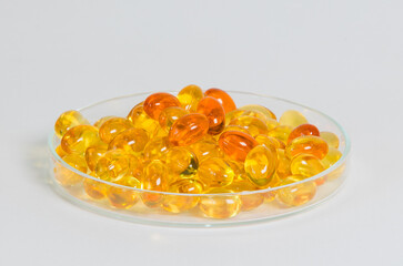 Close-up of yellow gel capsules filled in a transparent glass dish. Conceptual image for omega-3, fish oil, and nutritional health supplements with a clean, minimal medical background.