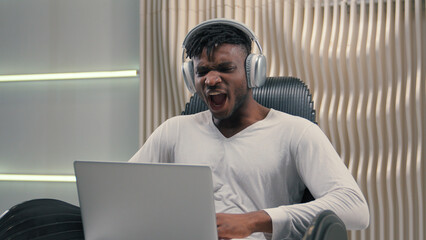African American ethnic cyber man in white futurism studio indoors business male user gamer hacker businessman guy futuristic in headphones win laptop success achieve computer good news amazed wow