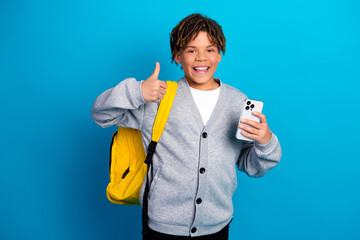 Happy schoolboy holding a smartphone and showing a thumbs up gesture on a blue background