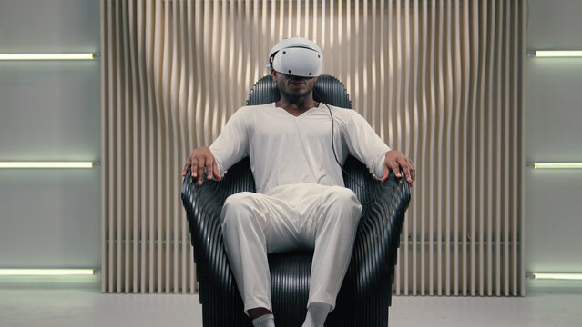 African American gamer guy male man put on virtual reality headset 3d VR helmet indoors playing interactive game watching simulation immersive digital experience modern technology futuristic room