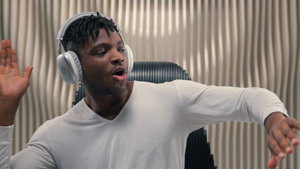 African American ethnic cyber man in white futurism studio indoors singing happy party male guy futuristic put on wireless headphones earphones dancing listening music song listen audio sing dance