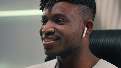 Close up happy smiling African American guy man ethnic male putting wireless headphones in ears listening music enjoying audio song in earphones positive relax in futuristic white studio futurism