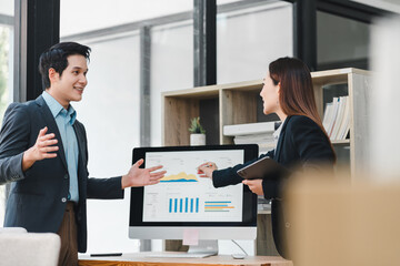 Business meeting two colleagues discussing data analysis office setting computer monitor displaying financial charts professional attire teamwork modern workspace focused atmosphere