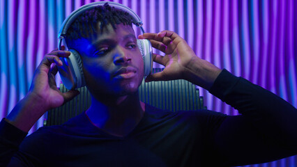Portrait calm dreaming relaxing tranquil peaceful resting African American man guy male user futuristic indoor futurism listening music in modern headphones listen audio song earphones sound dark room