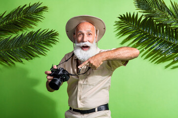 Photo of amazed excited old traveler man hold photo camera point advertise wear safari suit isolated green color background
