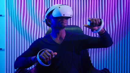 Cyber gamer African American man in VR glasses play virtual reality game in neon futuristic space indoors dark blue room guy male cyberpunk fashion gaming innovation playing using 3d simulation helmet