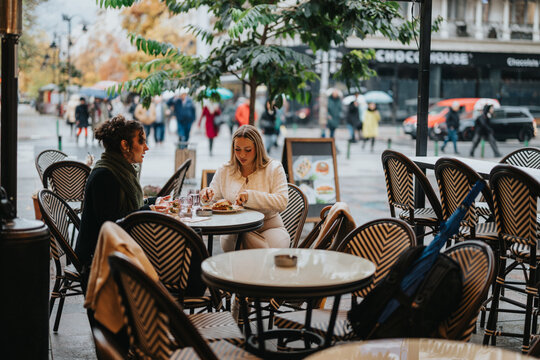 Two people share a meal at an outdoor cafe, surrounded by an urban and rainy ambiance. The cozy atmosphere reflects warmth and social connection during a cool, drizzly day. - Powered by Adobe
