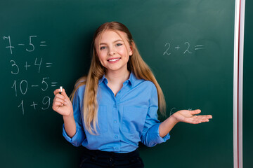 Smiling schoolgirl in blue shirt solving math problems on classroom chalkboard promoting education and learning concepts.