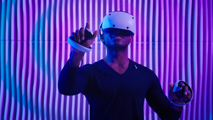Smiling happy African American man in VR glasses play virtual reality game in neon futuristic space browsing interactive future software interface guy male cyberpunk innovate simulation helmet working