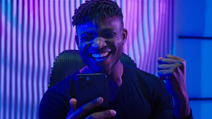 African American man guy male indoors futuristic innovation cyberspace neon lights winning with mobile phone bet casino online crypto win victory champion celebrate yelling happy video game addict