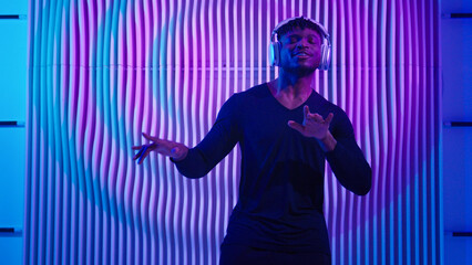 Happy smiling free enjoying glad moving dancing African American man listen musical mix in headphones move active smile dance listening music in dark blue futurism space male guy futuristic concept