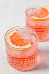 A refreshing negroni rosa cocktail served in a textured glass with ice, garnished with a slice of pink grapefruit, set against a light background. Summer party drink recipe, beverages menu.