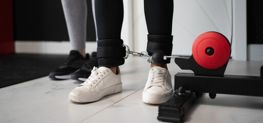Close-up of female athlete's legs wearing ankle weights, performing exercises with cable machine in...