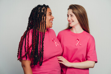 Two smiling women supporting breast cancer awareness, wearing pink ribbon
