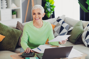Happy senior woman with grey hair calculating finances at home, enjoying a productive and...