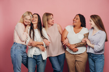Five diverse women embracing and laughing together on pink background