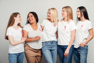 Diverse women embracing and smiling, showing pink ribbons for breast cancer awareness
