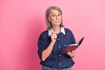Confident Mature Woman with Glasses Holding Notebook and Pen on Pink Background Wearing Stylish...