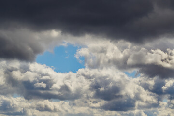 A small glimpse of blue sky in a wall of gray cumulus clouds in the sky, gray clouds, background, change in weather.