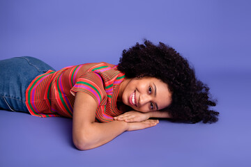 Young woman lying on a purple background in casual attire with vibrant t-shirt, smiling warmly and...