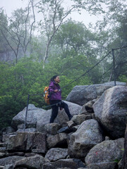 Hiker navigating rocky terrain in a lush forest in Norway on a misty day