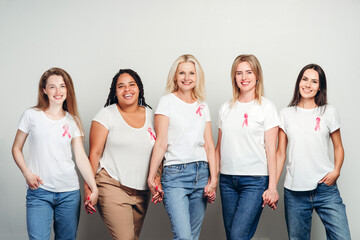 Smiling women holding hands wearing pink ribbon for breast cancer awareness