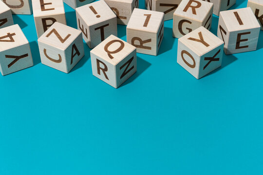 Close-up photo of wooden blocks with alphabet letters. Minimalist photo of wooden cubes with letters on turquoise blue background with copy space. Preschool, back to school and education concepts.