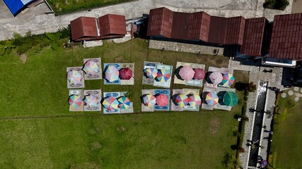 Vibrant top-down aerial view of colorful picnic setups with umbrellas and carpets on a manicured green lawn for outdoor leisure