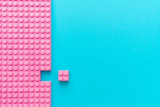 Bright pink plastic blocks on turquoise blue background with copy space as concept of missing fragment, ideal fit, out of the crowd, think different.