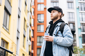 Bearded young businessman holding coffee cup outdoors.