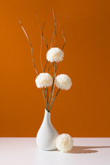Flores de crisantemo blancas decorativas en un jarrón blanco sobre fondo naranja	
