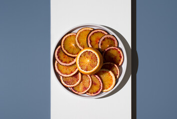 Rodajas de naranjas sanguinas en un plato blanco sobre un fondo blanco y azul. Vista superior