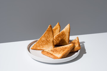 Triángulos de pan tostado dorados para sándwiches en un plato blanco sobre un fondo gris