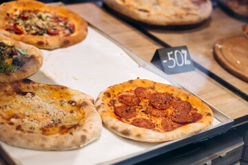 Pizzas displayed for sale in a shop window, close-up of delicious fast food.