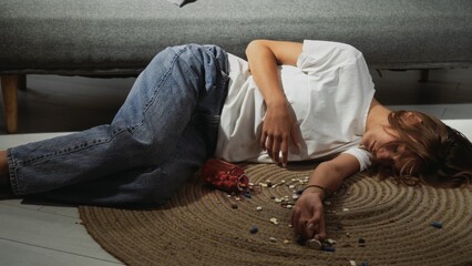 A young woman lies in front of a couch with various pills