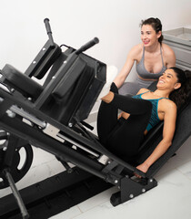 Woman doing leg press exercise with personal trainer assisting