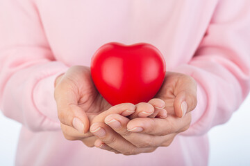 Close-up of hands gently holding a red heart symbol, wearing a pink sweater. Isolated on white background, representing love
