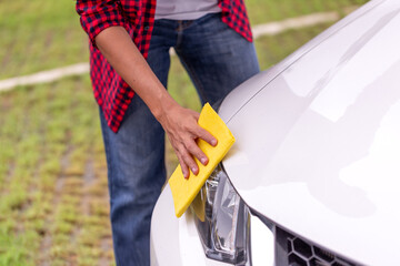 Man cleaning the front of a white car with a yellow microfiber cloth, focusing on the headlight and...